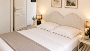 A bedroom with a bed, bedside tables, a nightstand, a door, and two framed pictures on the wall. - LE JASMIN 1-Bedroom Apartment, Sleeps 4 (Serra-di-Ferro)