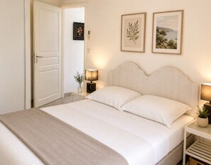 Ein Schlafzimmer mit einem Bett, Nachttischen, einem Tür und zwei gerahmten Bildern an der Wand.