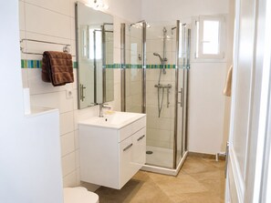 Ein modernes Badezimmer mit einer Duschkabine, einem weißen Waschtisch mit Spiegel und einem Handtuchhalter.