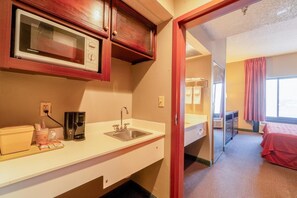 Ein Hotelzimmer mit Mikrowelle, Kaffeemaschine, Spüle und einem Bett mit roter Decke.
