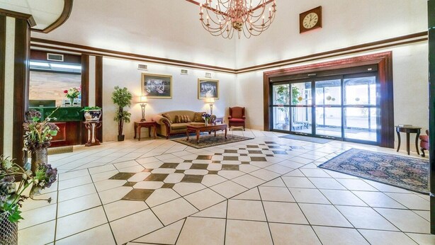 A lobby with a checkered floor, a chandelier, a reception desk, a sofa, and a large window. - 2 Queen Beds Suite Non-Smoking (Jonesboro, AR)