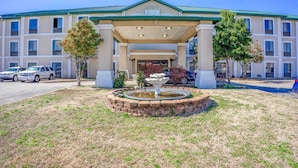 A hotel with a covered entrance, a fountain, and a parking lot. - 2 Queen Beds Suite Non-Smoking (Jonesboro, AR)