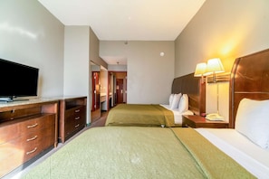 Ein Hotelzimmer mit Fernseher, zwei Betten mit grünen Bettdecken, einer Holzkommode, einem Nachttisch mit Lampe und einem durchgegangenen Tür angedeuteten Badezimmer.