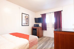 Una habitación con cama, escritorio, televisor y ventana con cortinas.