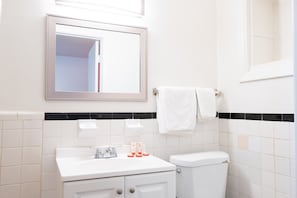 Un baño con lavamanos blanco, espejo, inodoro y toallero.