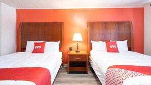 A hotel room with two beds, a nightstand with a lamp, and a red and white color scheme. - Jonesboro |2 Queen Bed (Jonesboro)