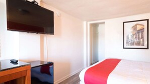 Ein Hotelzimmer mit Bett, Schreibtisch, Fernseher und einem gerahmten Bild an der Wand.