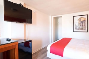 Quarto de hotel com uma cama, uma escrivaninha, televisão e um quadro na parede.