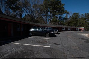 A motel with a row of rooms, a parking lot, and trees in the background. - Jonesboro | King Bed (Jonesboro)