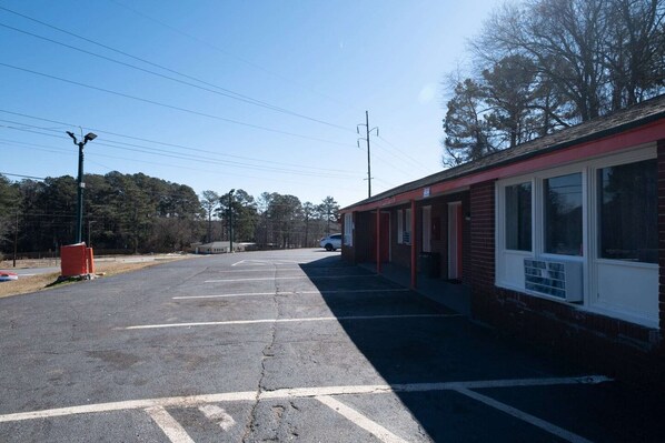 A parking lot with a building featuring a red exterior and large windows. - Jonesboro | King Bed (Jonesboro)