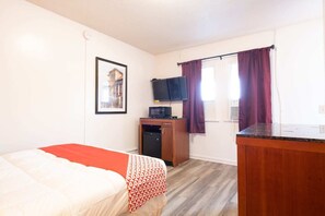 Quarto com cama, escrivaninha, televisão e janela com cortinas.
