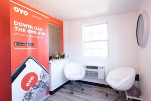 Habitación de hotel con un gran anuncio de la aplicación OYO, una ventana, una silla blanca y un reloj fijado a la pared.