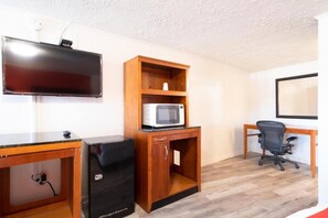 Una habitación con televisión de pantalla plana, microondas, escritorio, silla y archivador.