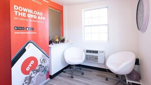 A hotel room with a large OYO app advertisement, a window, a white chair, and a wall-mounted clock. - Premium King Bed | Jonesboro (Jonesboro)