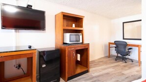 A room with a flat-screen TV, a microwave, a desk, a chair, and a filing cabinet. - Premium King Bed | Jonesboro (Jonesboro)