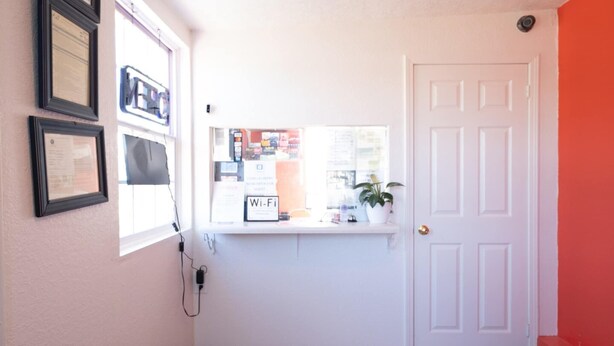 A hallway with a white door, a window with a Wi-Fi sign, and framed certificates on the wall. - Premium King Bed | Jonesboro (Jonesboro)
