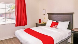 Una habitación de hotel con una cama grande, una mesita de noche con teléfono y una ventana con cortinas rojas.