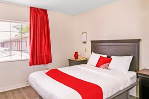 A hotel room with a bed, a nightstand, a red curtain, a window, and a view of the outside.