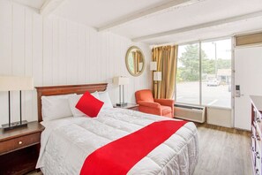 Ein Hotelzimmer mit Bett, Stuhl, Fenster, Spiegel und Tür.