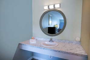 Un baño con lavabo de mármol, espejo redondo y tocador iluminado.