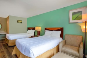 Habitación de hotel con dos camas, una silla, una mesita de noche con lámpara y un cuadro en la pared.