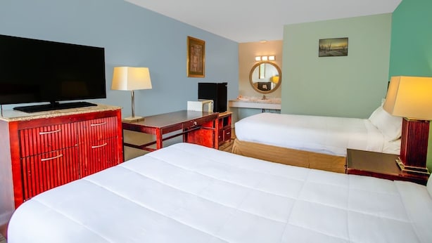 Habitación de hotel con dos camas, televisión, escritorio, espejo y lámpara.