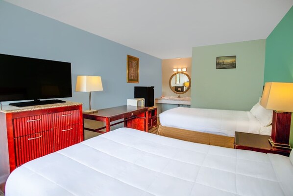 A hotel room with two beds, a TV, a desk, a mirror, and a lamp.