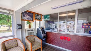 Zona de recepción con mostrador de registro, dos sillones estampados, un equipo de aire acondicionado y un letrero en la pared con el logotipo 'OYO'.