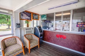 Zona de recepción con mostrador de registro, dos sillones estampados, un equipo de aire acondicionado y un letrero en la pared con el logotipo 'OYO'.