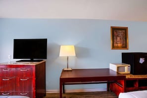 A hotel room with a TV, a lamp, a microwave, a framed picture on the wall, and a wooden table.