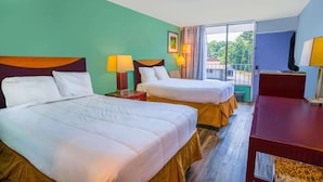 Habitación de hotel con dos camas, un escritorio y una ventana con vistas a zonas verdes.