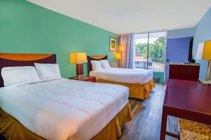 Habitación de hotel con dos camas, un escritorio y una ventana con vistas a zonas verdes.