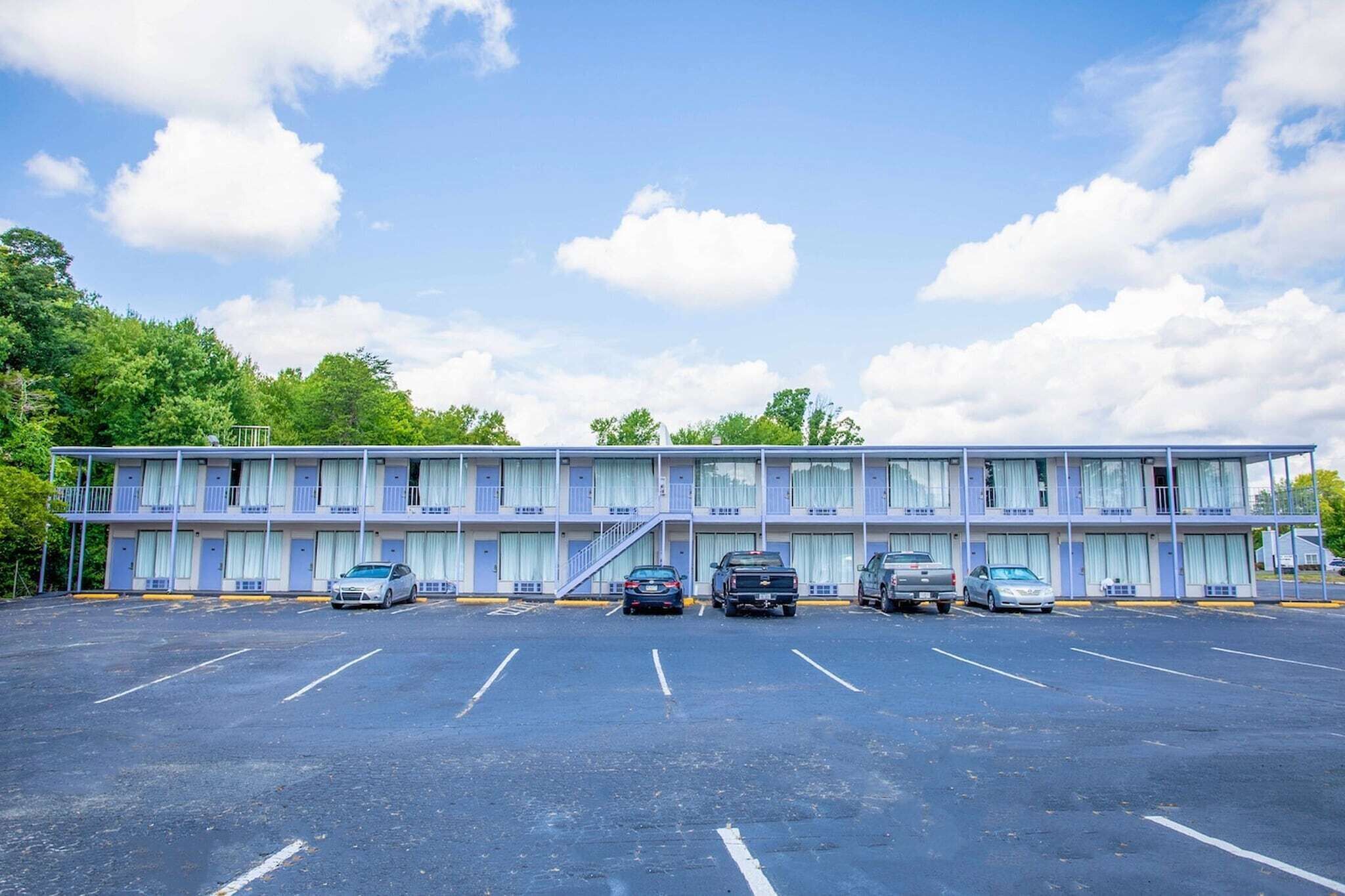 A motel with a parking lot, multiple rooms, and a staircase leading to the upper floor.