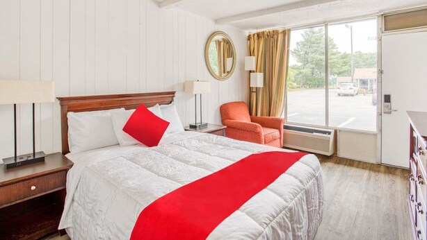 A hotel room with a bed, a chair, a mirror, and a window with curtains.
