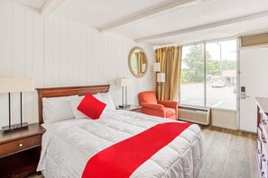 A hotel room with a bed, a chair, a mirror, and a window with curtains.