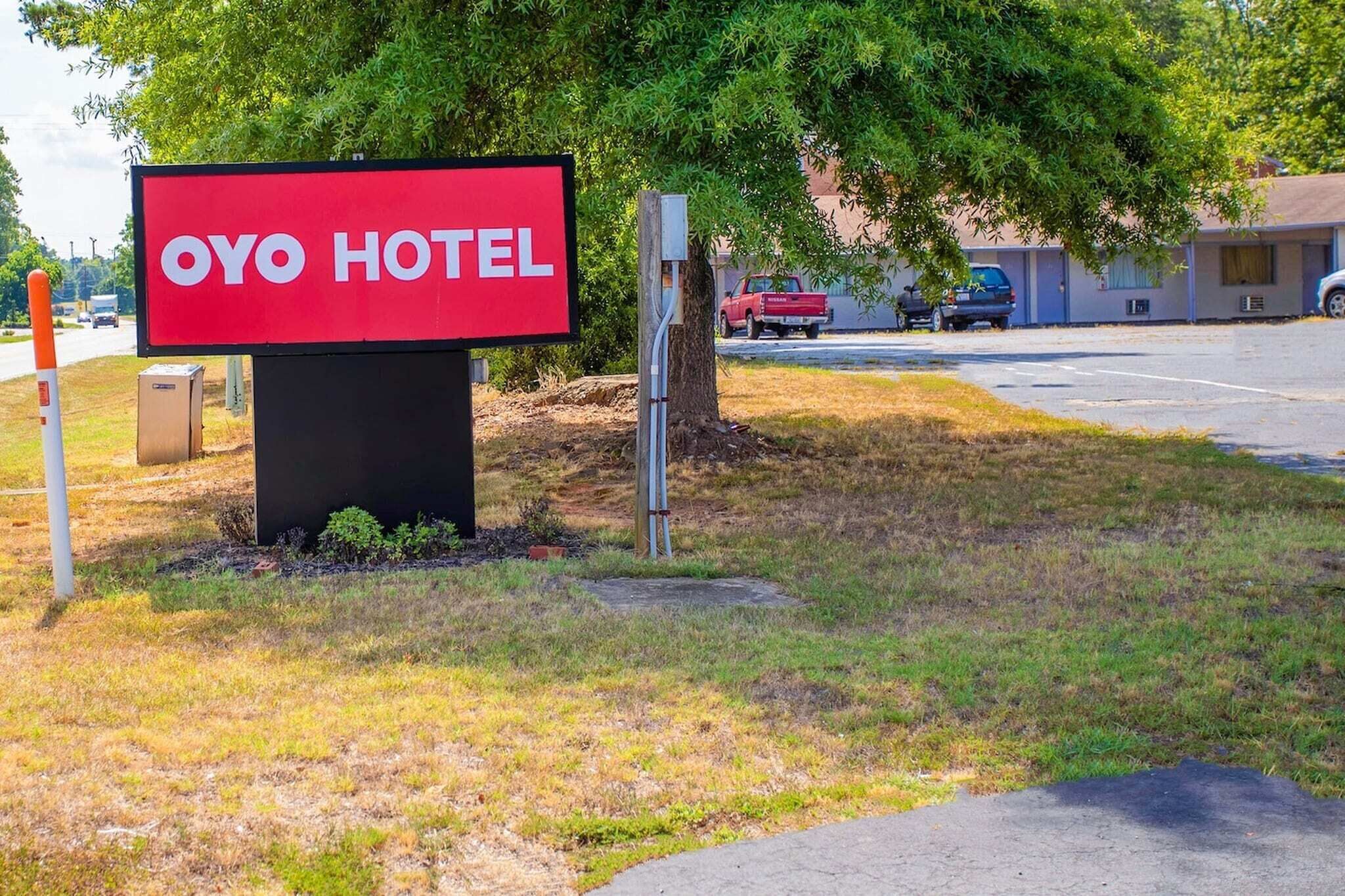 OYO-hotellin kyltti, josta avautuu selkeä näkymä ympäröivään alueeseen, mukaan lukien parkkipaikka ja taustalla oleva rakennus.