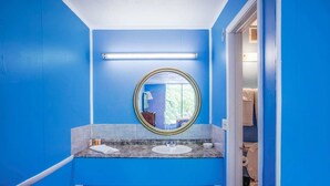 A bathroom with blue walls, a round mirror, two sinks, and a visible toilet.