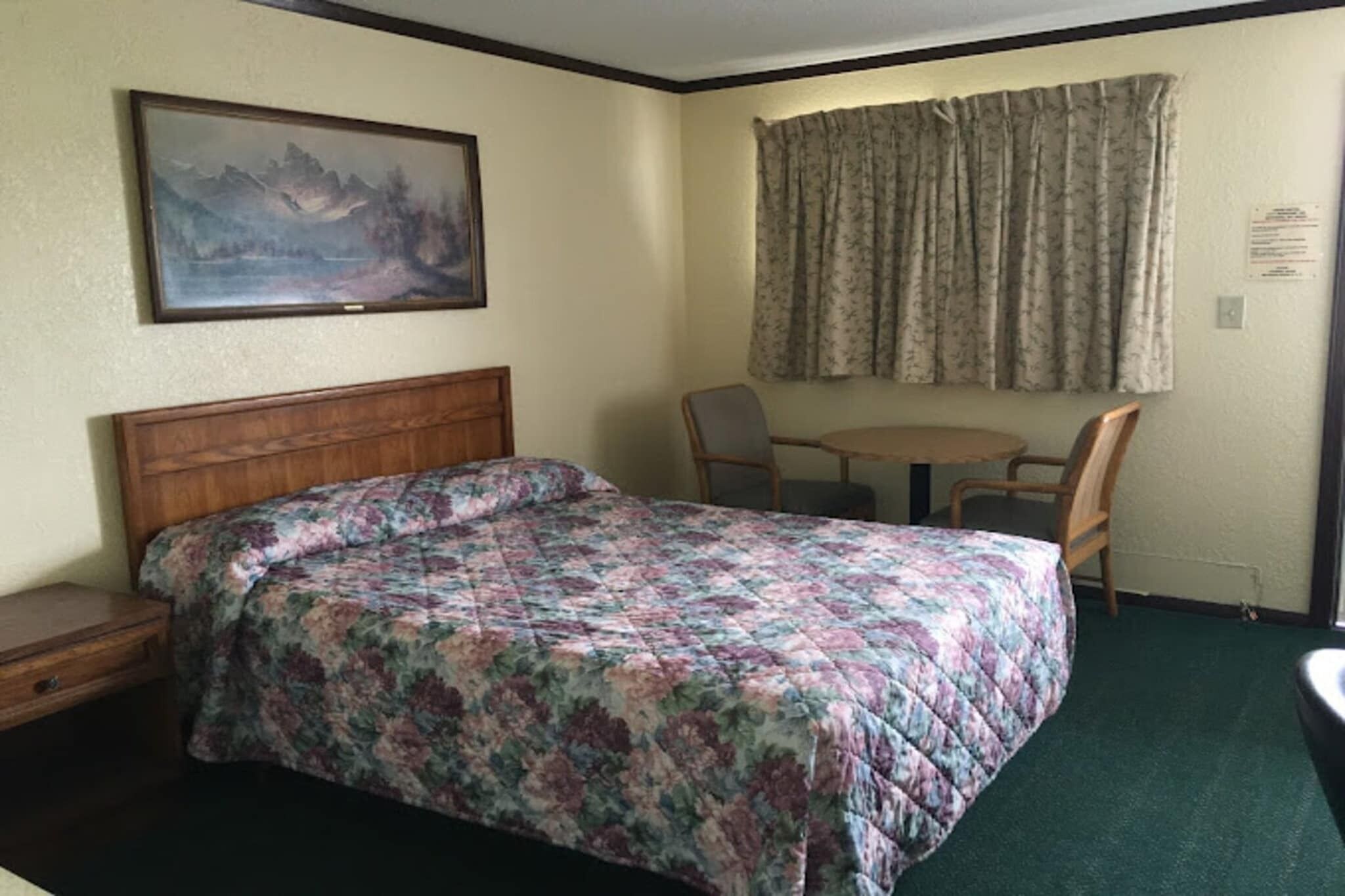 A room with a bed, a desk, a chair, a window with curtains, and a painting on the wall.
