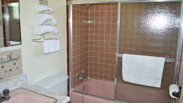A bathroom with a pink bathtub, a glass shower enclosure, and a towel rack with folded towels.