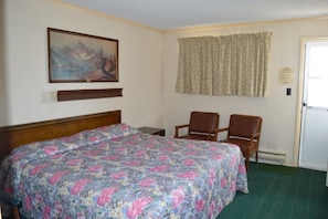 Ein Hotelzimmer mit einem Bett, zwei Stühlen, einem Gemälde, einem Vorhang und einer Tür.
