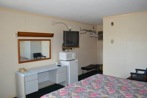 Une petite pièce comprenant un lit, un bureau, une télévision, un miroir et une chaise.