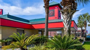 Un edificio rojo con techo verde, palmeras y un estacionamiento.
