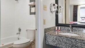 A bathroom with a white toilet, a shower, a sink with a granite countertop, and a mirror.