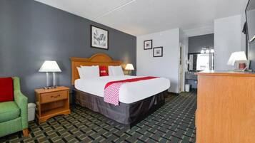 A hotel room with a bed, bedside tables, a green chair, and a wooden desk.