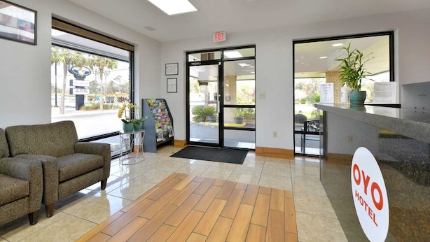 A hotel reception area with a sofa, a reception desk, a plant, and a door leading outside. - 2 Full Bed | Accessible (Lake Park GA)