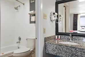 A bathroom with a white toilet, a shower, a sink with a granite countertop, and a mirror. - 2 Full Bed | Accessible (Lake Park GA)
