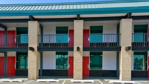A multi-story building with a flat roof, red doors, and a parking lot in front.