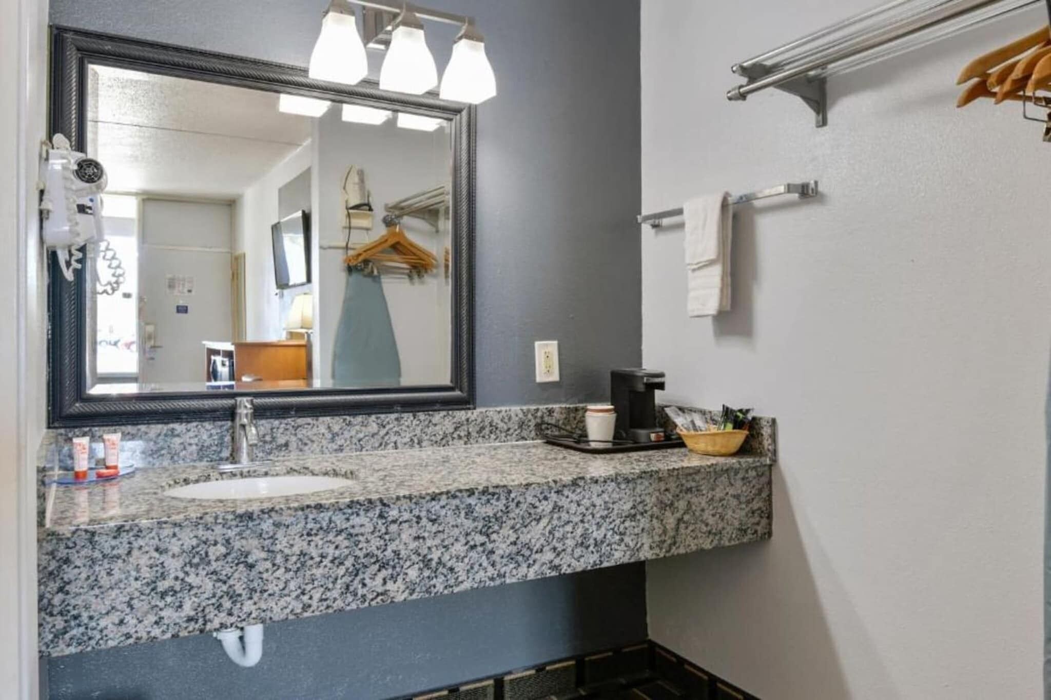A bathroom with a granite countertop sink, a large mirror, a towel rack, and a coffee maker.