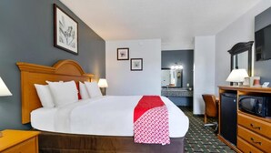 A hotel room with a bed, bedside table, lamp, dresser, microwave, and a mirror.