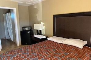 Ein Hotelzimmer mit Bett, Nachttisch, Lampe, Fernseher und einer Badezimmertür.